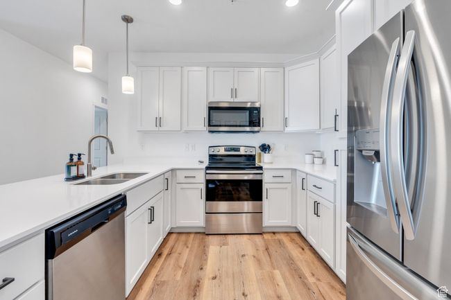 Kitchen with white cabinets, decorative light fixtures, a sink, appliances with stainless steel finishes, and light wood finished floors | Image 6