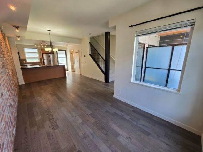 Unfurnished living room featuring dark wood finished floors, a chandelier, baseboards, and stairway | Image 6