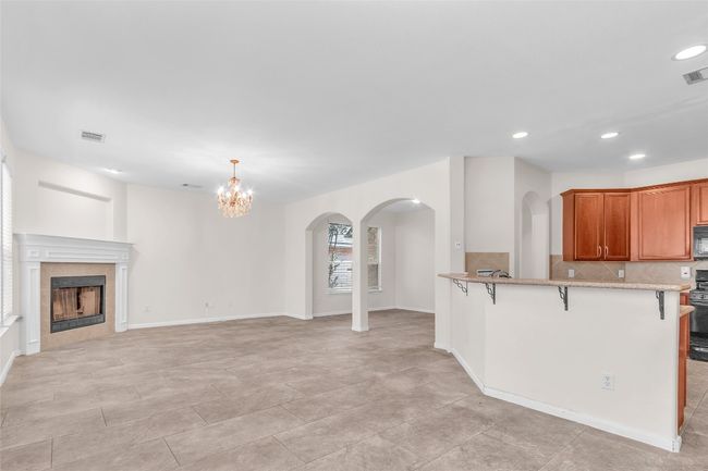 Kitchen with a kitchen bar, backsplash, a tile fireplace, brown cabinets, and arched walkways | Image 7