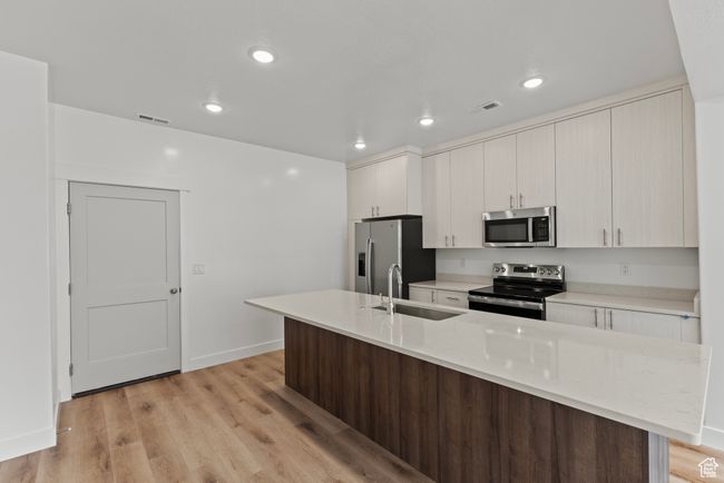 Kitchen with a sink, stainless steel appliances, a center island with sink, light wood-style flooring, and visible vents | Image 5
