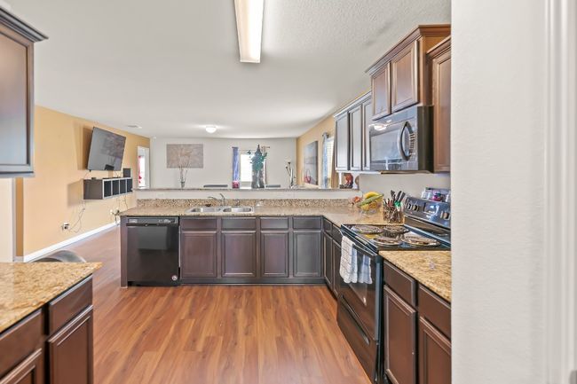 Kitchen featuring black appliances, sink, kitchen peninsula, light wood-type flooring, and light stone counters | Image 6
