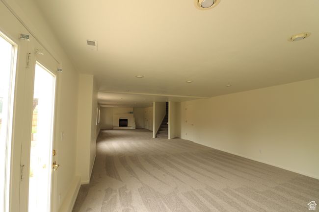 Unfurnished living room featuring light colored carpet, stairs, a fireplace with raised hearth, and recessed lighting | Image 13