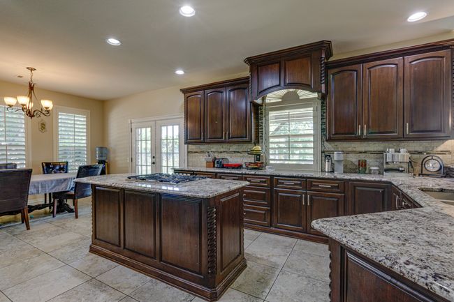 Kitchen with decorative backsplash, light stone counters, stainless steel gas stovetop, recessed lighting, and a chandelier over the breakfast area. | Image 12