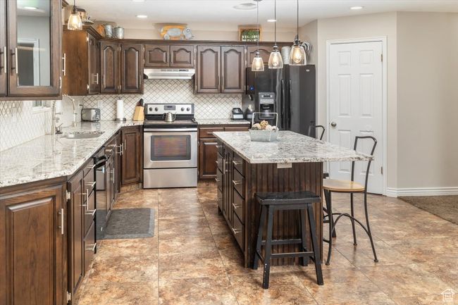 Kitchen with electric stove, black fridge with ice dispenser, a kitchen island, sink, and light tile patterned flooring | Image 7