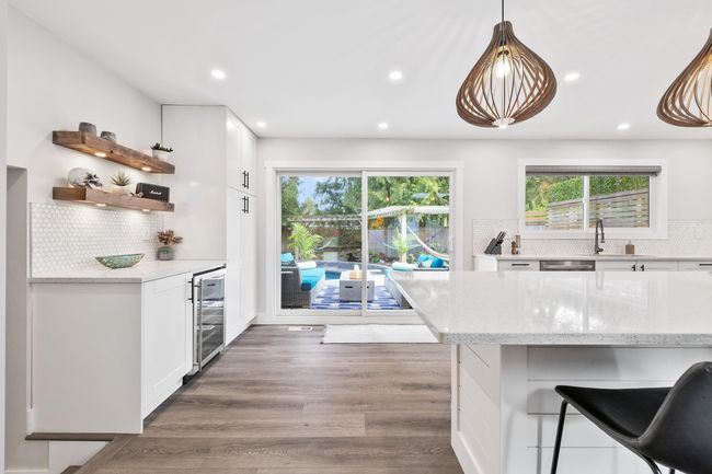 Kitchen featuring light stone counters, white cabinetry, backsplash, wine cooler, and wood finished floors | Image 12
