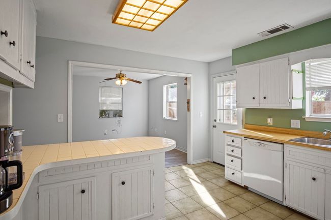 Kitchen featuring dishwasher, light tile patterned flooring, ceiling fan, light countertops, and white cabinetry | Image 6