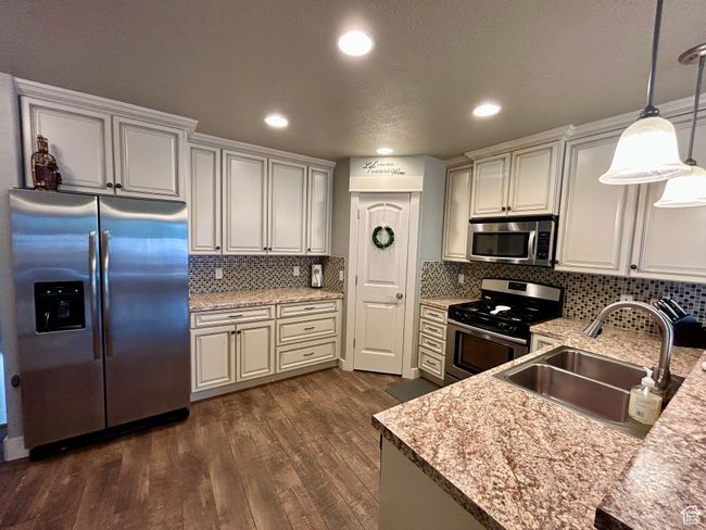 Kitchen with appliances with stainless steel finishes, a sink, dark wood-style flooring, pendant lighting, and decorative backsplash | Image 10