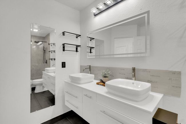 Full bath featuring double vanity, dark tile patterned floors, tiled shower, backsplash, and a textured wall | Image 14