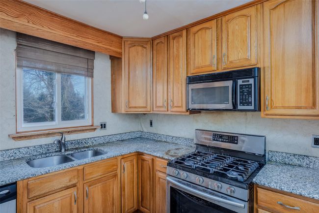 Kitchen with appliances with stainless steel finishes, brown cabinetry, a sink, and light stone countertops | Image 12