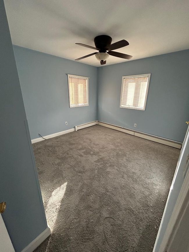 Carpeted spare room featuring ceiling fan, baseboard heating, and plenty of natural light | Image 14