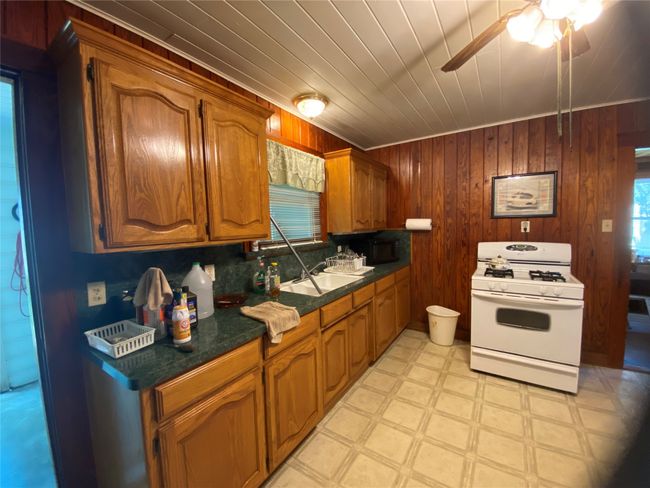 Kitchen featuring white gas range, light flooring, a ceiling fan, dark countertops, and wood walls | Image 13