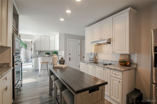 Kitchen featuring oven, decorative backsplash, under cabinet range hood, black electric cooktop, and light wood-type flooring | Image 11