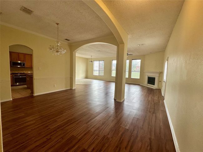 Unfurnished living room featuring a chandelier, a textured ceiling, dark wood-type flooring, a fireplace with raised hearth, and arched walkways | Image 4