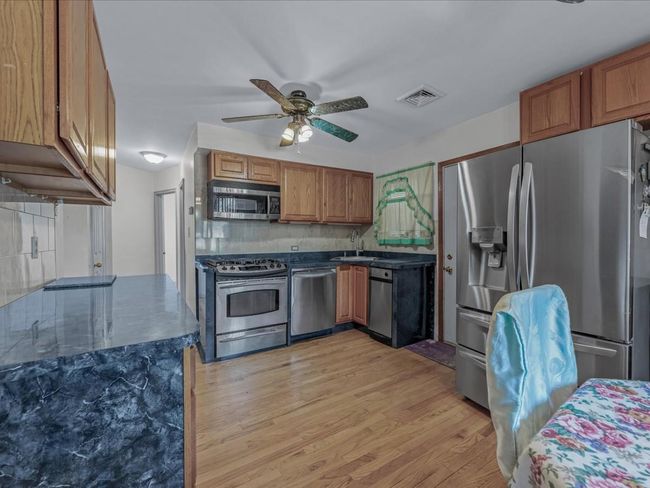 Kitchen with stainless steel appliances, ceiling fan, light wood-type flooring, brown cabinetry, and dark stone counters | Image 7
