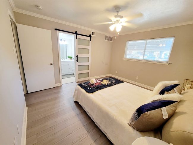 Bedroom with light wood-type flooring, a barn door, ceiling fan, and ornamental molding | Image 11