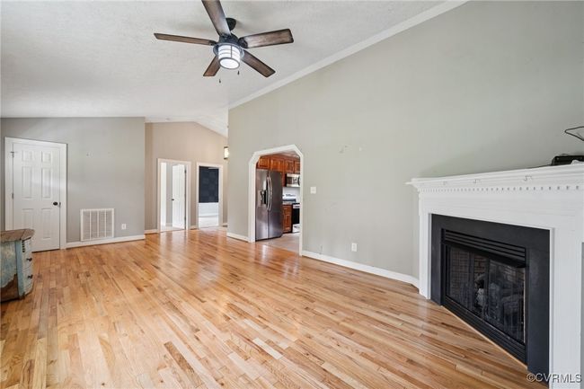 Unfurnished living room featuring lofted ceiling, ceiling fan, a fireplace, light wood finished floors, and baseboards | Image 6