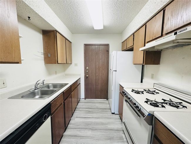 Kitchen featuring white appliances, light countertops, light wood-style flooring, under cabinet range hood, and a textured ceiling | Image 11