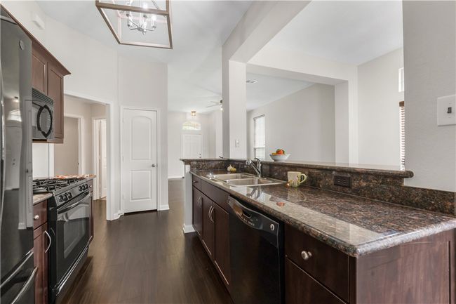 Kitchen featuring black appliances, a sink, dark wood-style flooring, dark stone counters, and dark brown cabinetry | Image 8