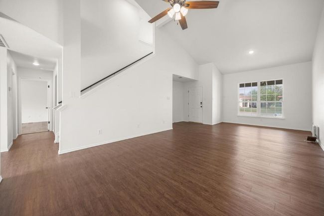Unfurnished living room with dark wood-style floors, high vaulted ceiling, ceiling fan, and baseboards | Image 5