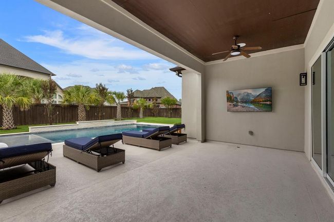 This covered patio is a true outdoor retreat—featuring views of the sparkling pool surrounded by lush palms. Perfect for relaxing poolside or hosting game-day gatherings in comfort and shade. | Image 38
