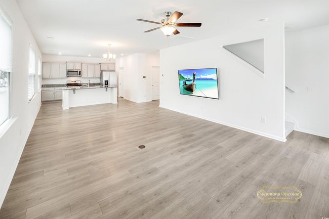 Unfurnished living room featuring a chandelier, ceiling fan, baseboards, light wood-type flooring, and stairway | Image 16