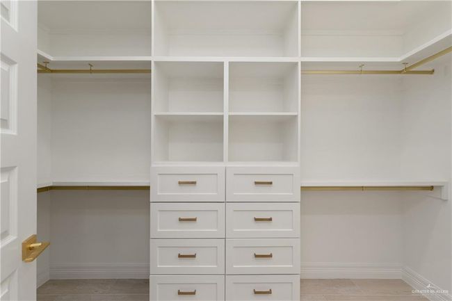 Spacious Primary ClosetThoughtfully designed closet with ample storage, custom drawers, open shelving, and dual hanging spaces with brass rods. | Image 21