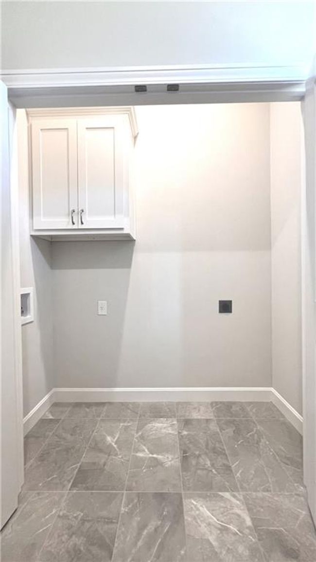 Laundry area sits within the master closet, featuring marble look tile flooring, hookup for an electric dryer, washer hookup, and cabinet space | Image 15