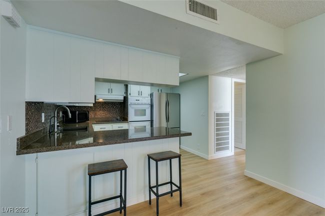 Kitchen featuring freestanding refrigerator, under cabinet range hood, a peninsula, light wood finished floors, and tasteful​​‌​​​​‌​​‌‌​‌‌​​​‌‌​​‌‌​‌​​​​​‌ backsplash | Image 21