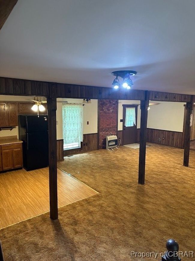 Unfurnished living room with wooden walls, light colored carpet, and heating unit | Image 9