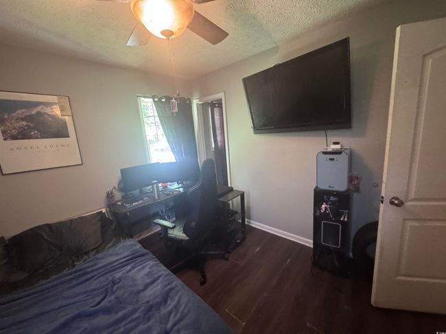 Bedroom with a textured ceiling, wood finished floors, a ceiling fan, baseboards, and a desk | Image 6