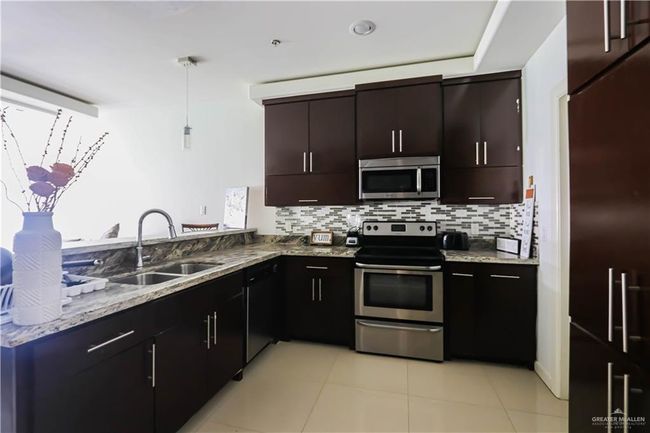 Kitchen featuring light stone counters, light tile patterned flooring, stainless steel appliances, a sink, and decorative backsplash | Image 8