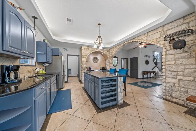Kitchen with arched walkways, a tray ceiling, open shelves, a sink, and blue cabinets | Image 9