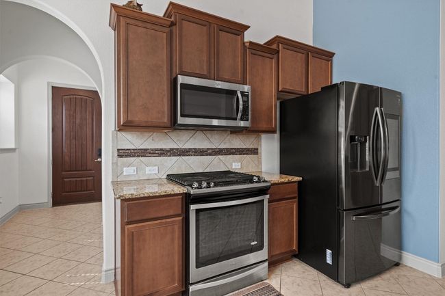 Kitchen with appliances with stainless steel finishes, baseboards, decorative backsplash, light stone counters, and light tile patterned floors | Image 5