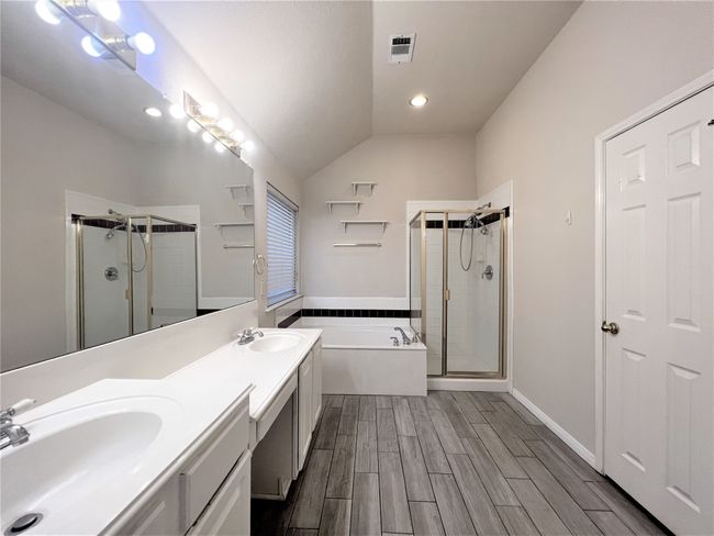 Bathroom featuring a stall shower, a bath, double vanity, wood finished floors, and vaulted ceiling | Image 11