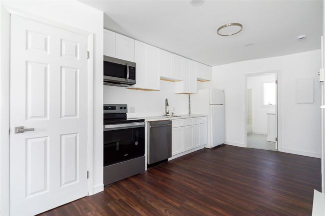 Kitchen with dark wood-style flooring, baseboards, white cabinets, light quartz countertops, and appliances with stainless steel finishes | Image 6