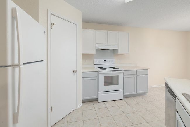 Kitchen featuring white appliances, under cabinet range hood, light countertops, light tile patterned flooring, and a textured ceiling | Image 12