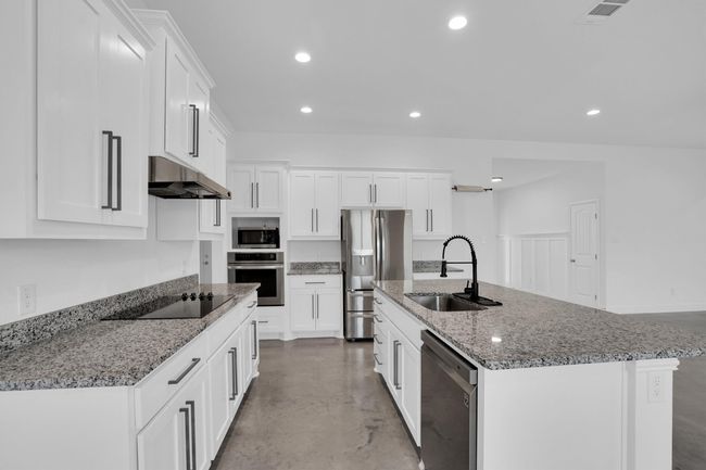 Kitchen featuring stainless steel appliances, a sink, under cabinet range hood, finished concrete floors, and white cabinetry | Image 18