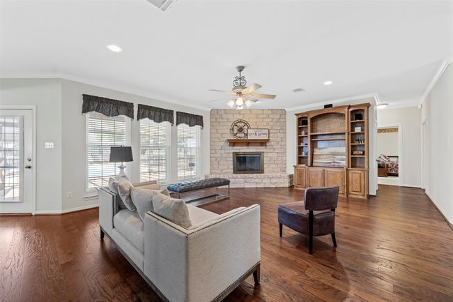 Living room featuring a ceiling fan, a fireplace, dark wood-type flooring, and ornamental molding | Image 6