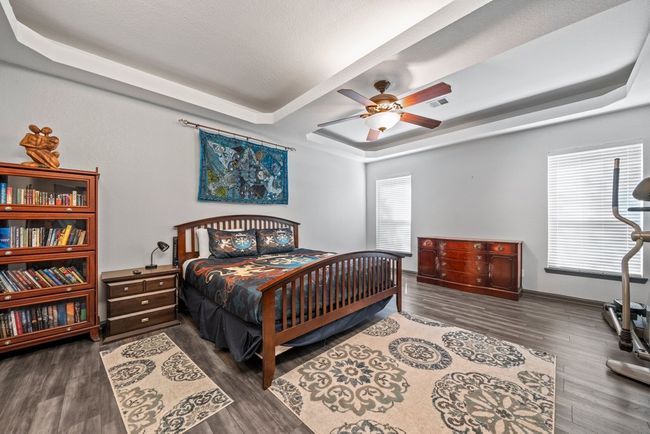 Bedroom with visible vents, baseboards, a ceiling fan, wood finished floors, and a tray ceiling | Image 15