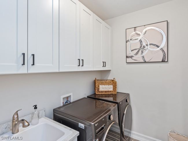 Efficiency meets style in this well-appointed laundry room featuring overhead cabinets, a laundry tub, and sleek front-load smart washer and dryer | Image 22