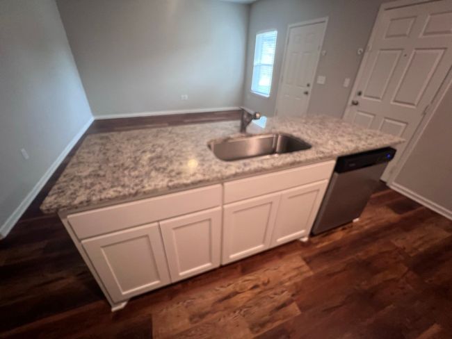 Kitchen featuring stainless steel dishwasher, a sink, dark wood-type flooring, white cabinetry, and light stone countertops | Image 19