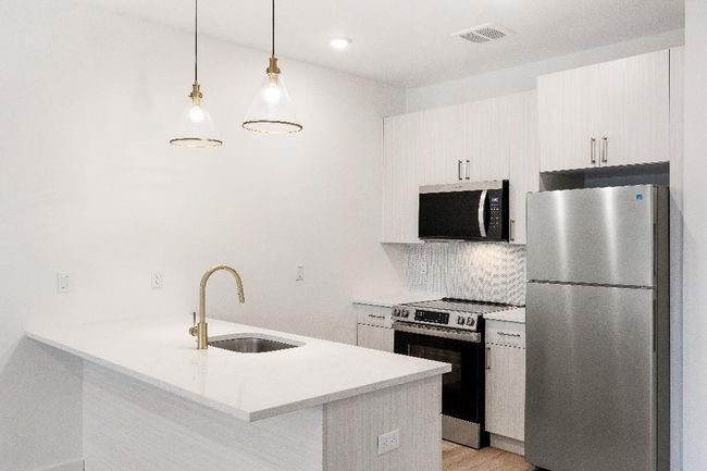 Kitchen featuring stainless steel appliances, a sink, light countertops, a peninsula, and backsplash | Image 32