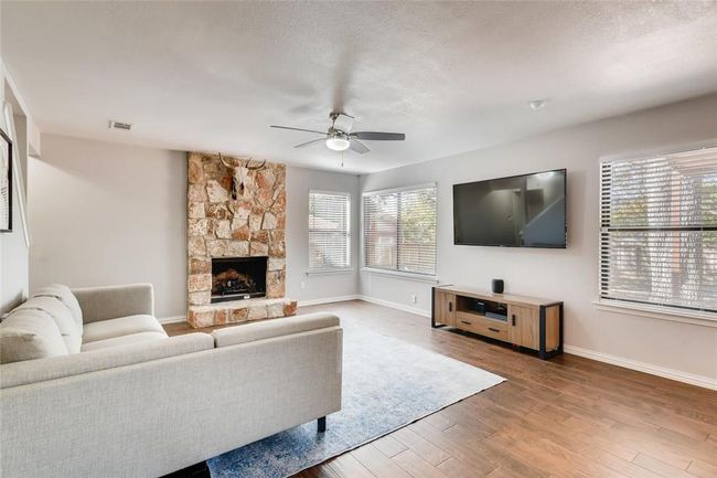 Living area with ceiling fan, baseboards, wood finished floors, and a stone fireplace | Image 4
