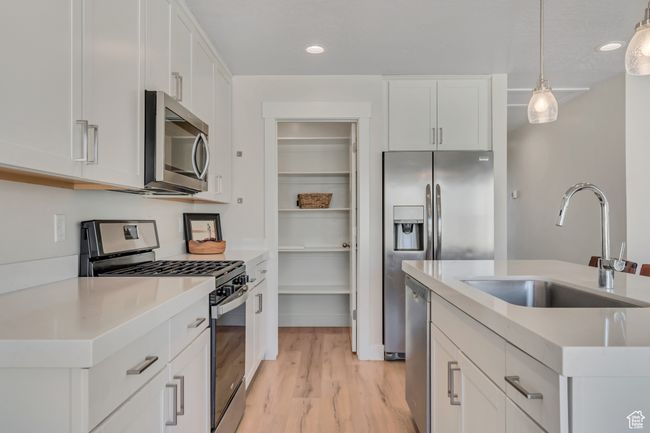 Kitchen featuring stainless steel appliances, hanging light fixtures, white cabinets, light wood-type flooring, and light countertops | Image 9