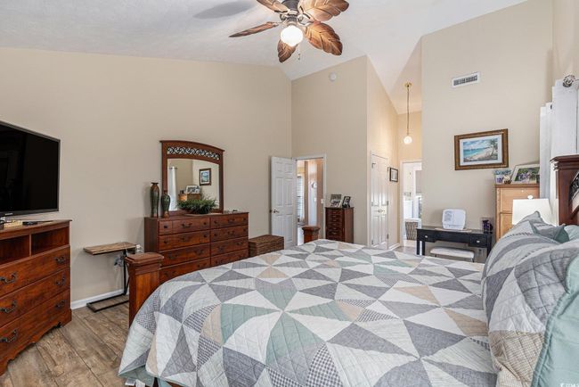 Bedroom featuring wood finished floors, high vaulted ceiling, baseboards, connected bathroom, and ceiling fan | Image 21