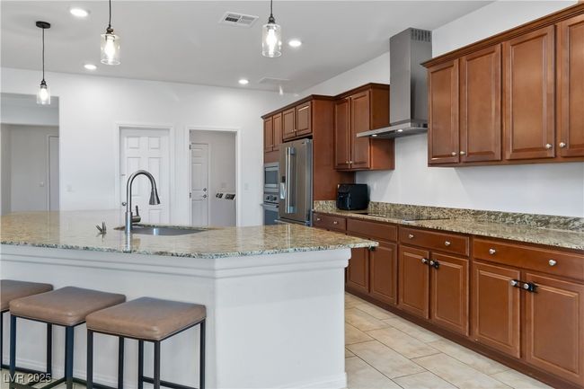 Kitchen featuring visible vents, appliances with stainless steel finishes, wall chimney range hood, a kitchen bar, and a sink | Image 21
