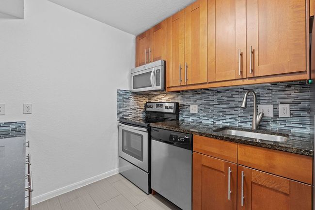 Kitchen with tasteful backsplash, baseboards, dark stone countertops, stainless steel appliances, and a sink | Image 11