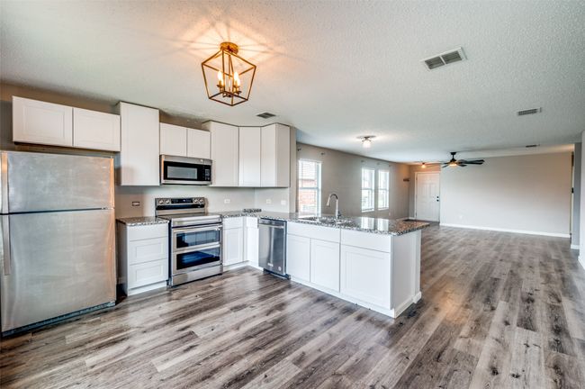 Kitchen featuring stainless steel appliances, a sink, a peninsula, wood finished floors, and a textured ceiling | Image 7