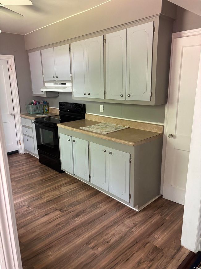 Kitchen with black range with electric stovetop, under cabinet range hood, dark wood-style flooring, white cabinets, and a ceiling fan | Image 9