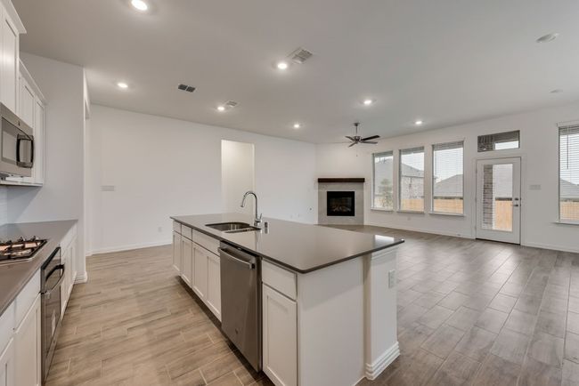 Kitchen featuring stainless steel appliances, a ceiling fan, a glass covered fireplace, light wood-style floors, and a kitchen island with sink | Image 6